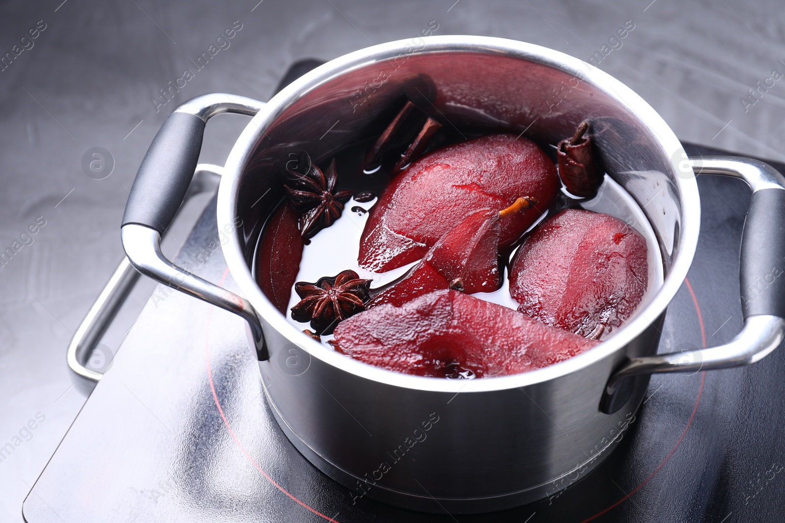 Photo of Tasty red wine poached pears and spices in pot on grey table, closeup