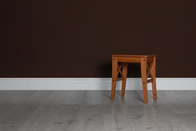 Photo of Stylish wooden stool near brown wall indoors. Space for text