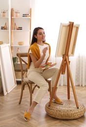 Beautiful young woman drawing on easel at home