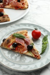 Tasty pizza with cured ham, olives, tomato and basil on white table