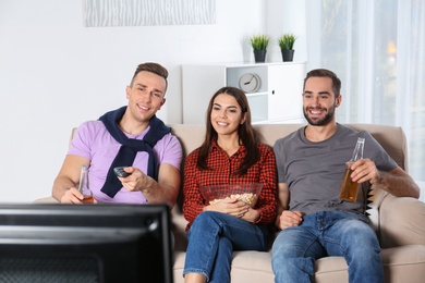 Young friends watching TV on sofa at home