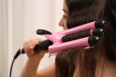 Photo of Young woman using modern curling iron against light background, focus on device