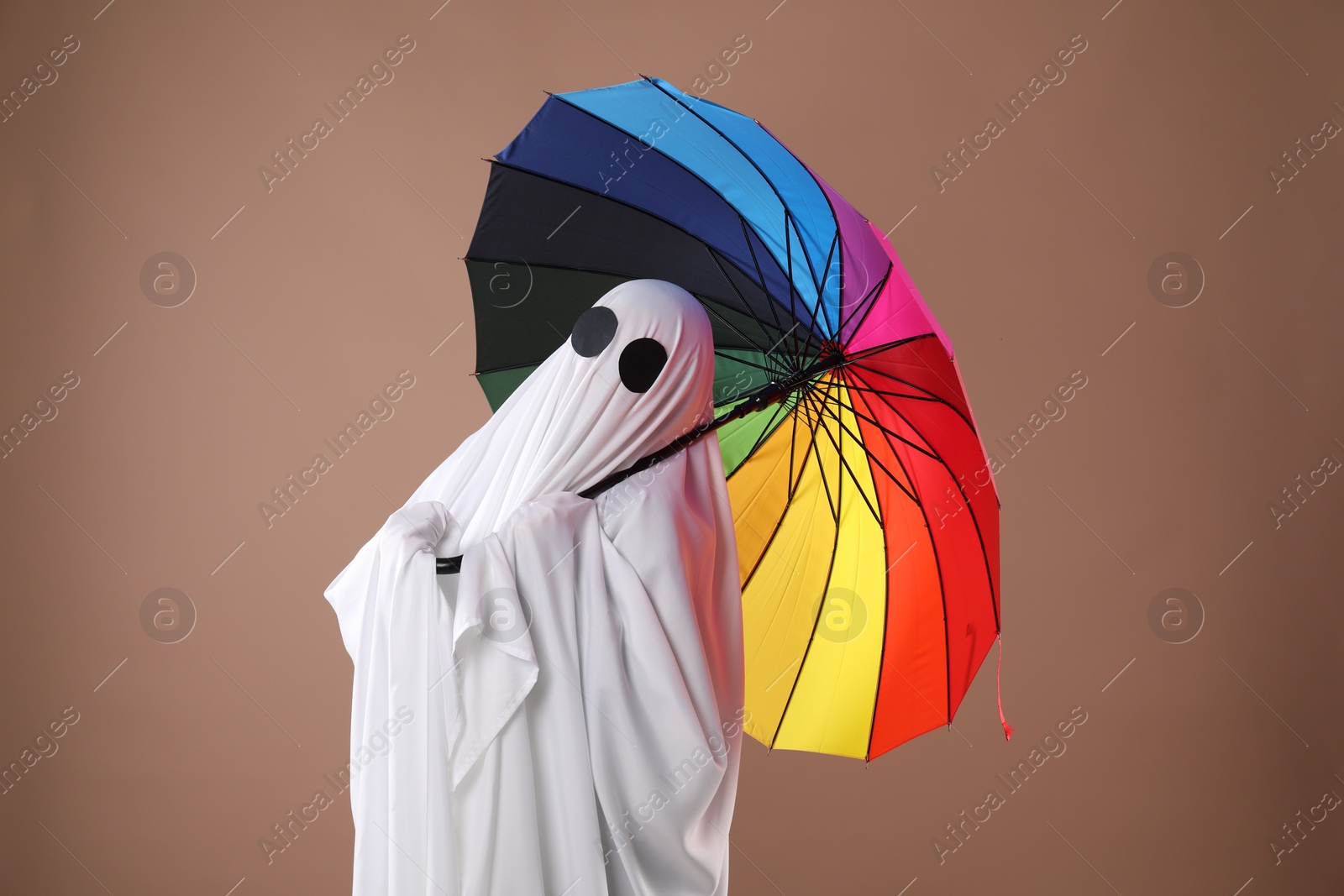 Photo of Person in ghost costume with rainbow umbrella on dark beige background