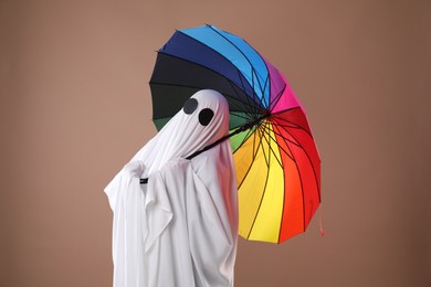 Photo of Person in ghost costume with rainbow umbrella on dark beige background