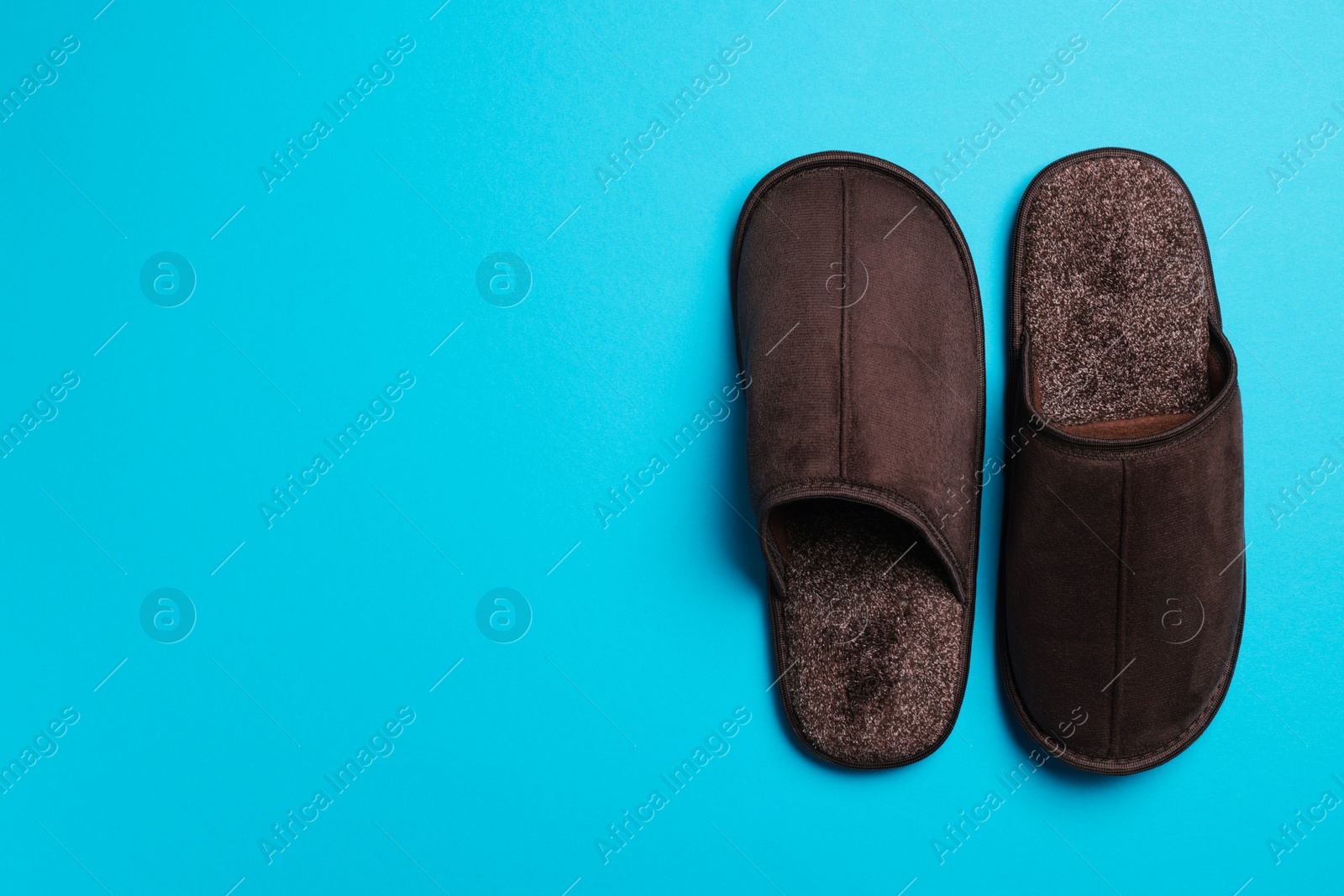 Photo of Pair of brown slippers on light blue background, top view. Space for text