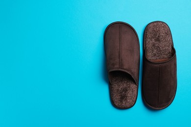 Photo of Pair of brown slippers on light blue background, top view. Space for text