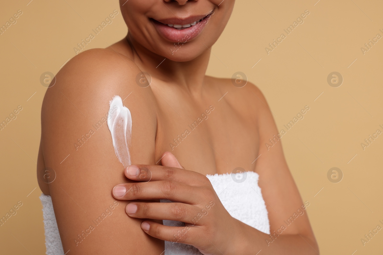 Photo of Young woman applying body cream onto shoulder on beige background, closeup