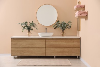 Photo of Modern bathroom interior with stylish mirror, eucalyptus branches, vessel sink and wooden vanity
