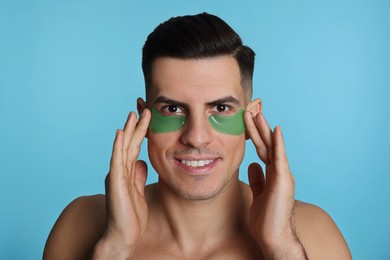 Photo of Man applying green under eye patches on light blue background