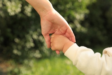 Daughter holding mother's hand in park, closeup. Happy family
