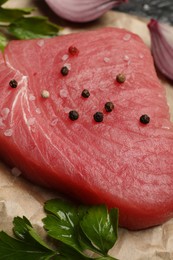 Photo of Raw tuna fillet with parsley and spices on parchment paper, closeup