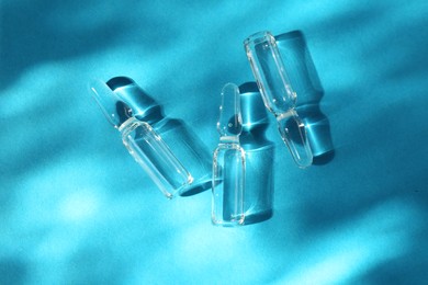 Skincare ampoules in sunlight on light blue background, top view