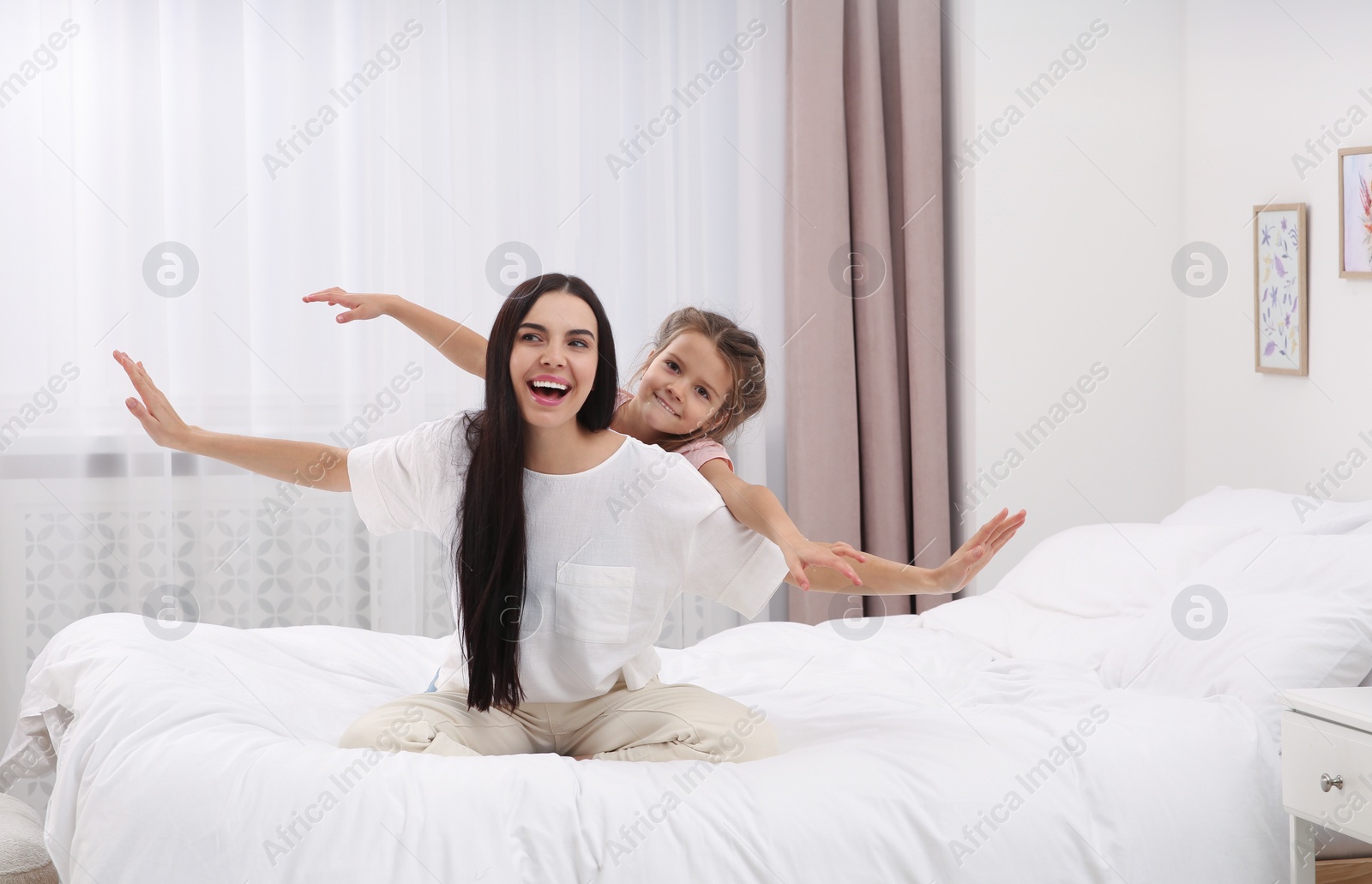 Photo of Happy woman and her daughter having fun on bed at home. Mother's day celebration