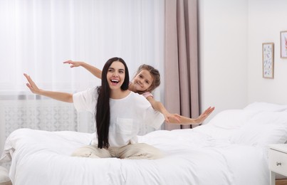 Photo of Happy woman and her daughter having fun on bed at home. Mother's day celebration