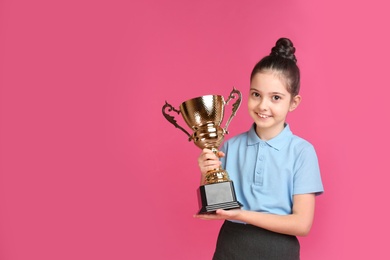 Photo of Happy girl in school uniform with golden winning cup on pink background. Space for text