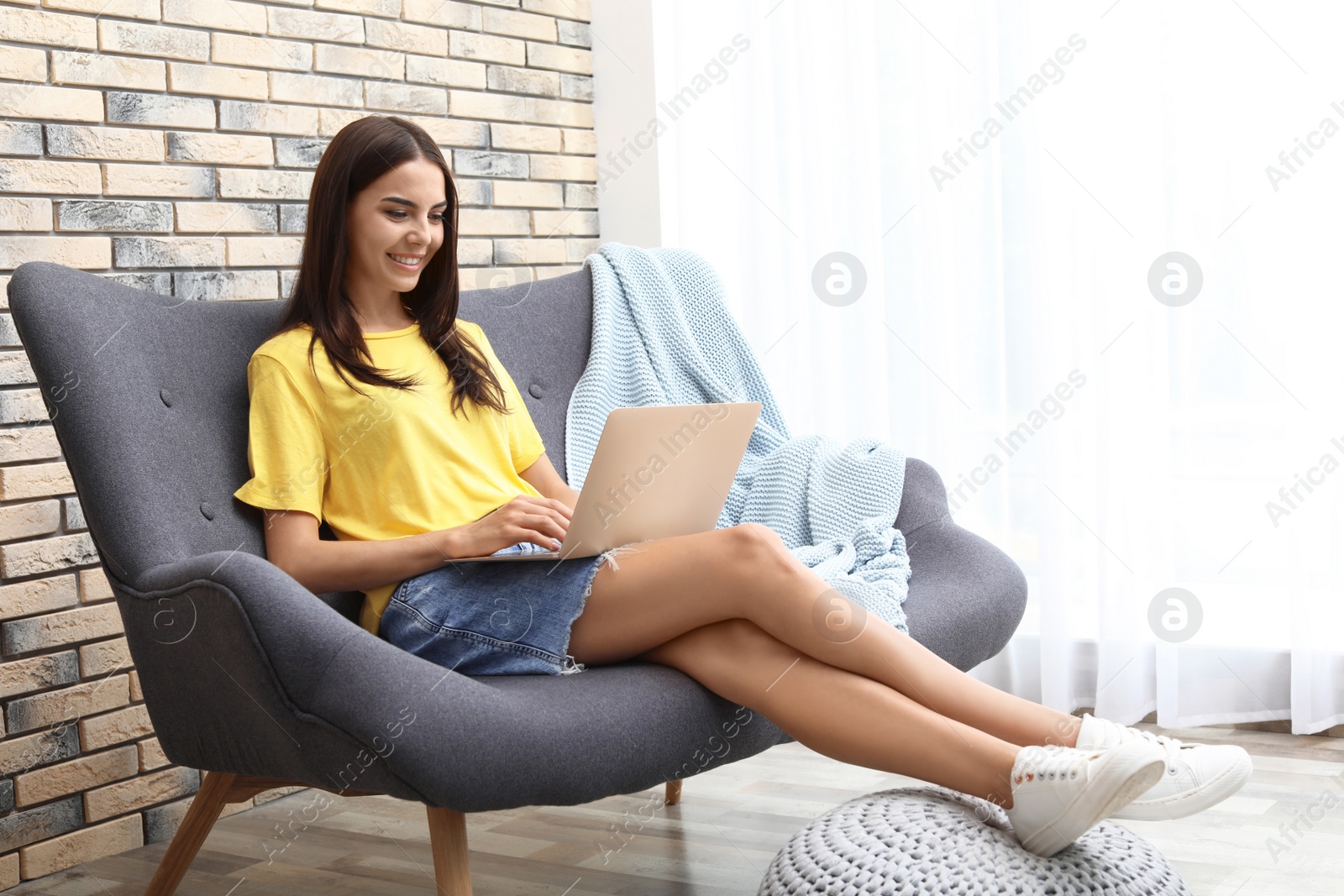 Photo of Young woman with modern laptop sitting on sofa at home