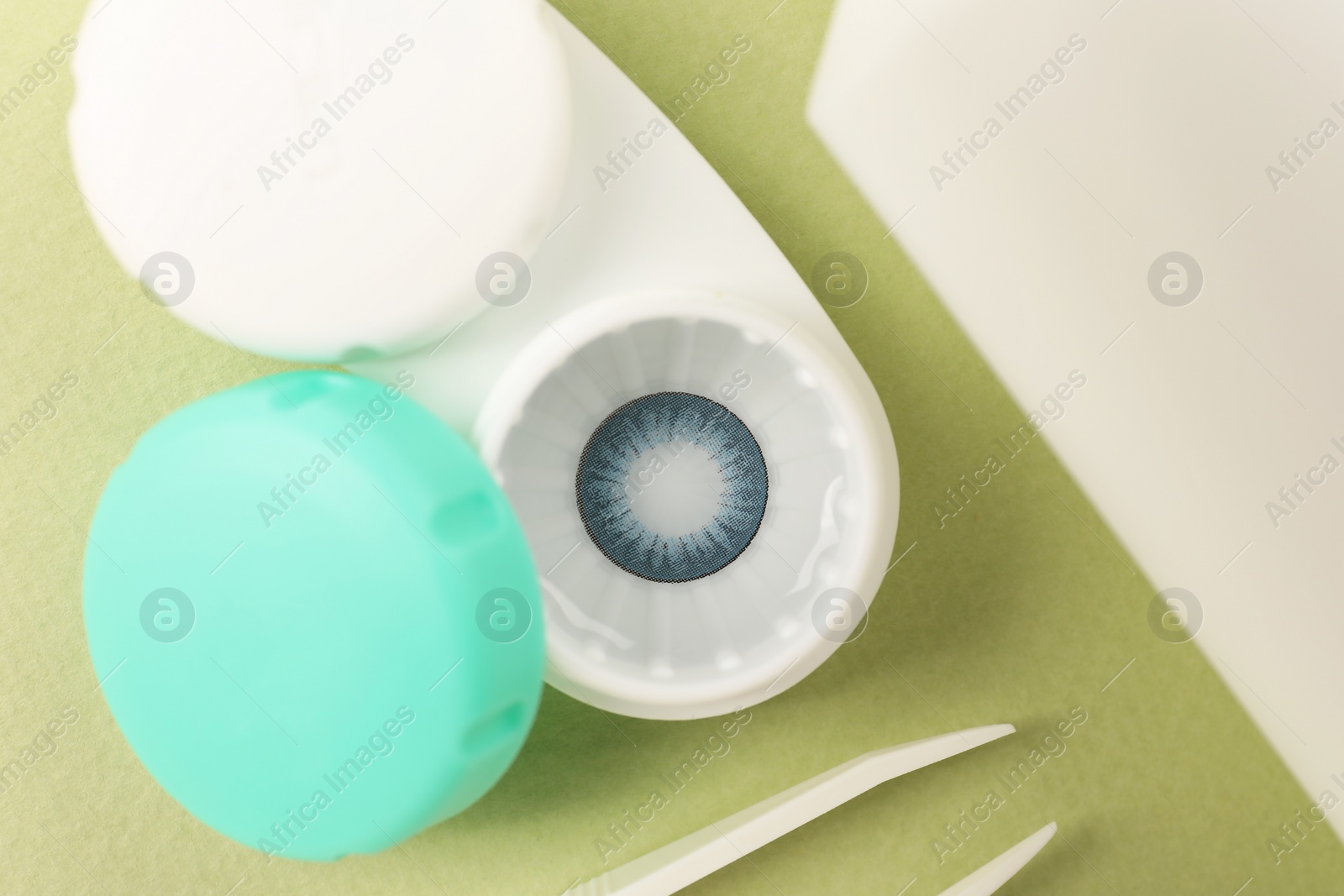 Photo of Case with blue contact lenses and tweezers on color background, flat lay