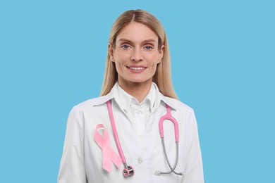 Photo of Doctor with pink ribbon and stethoscope on light blue background. Breast cancer awareness