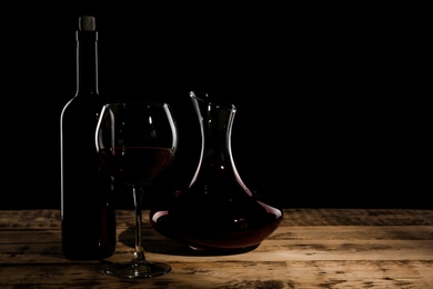 Photo of Decanter, glass and bottle with red wine on table against dark background