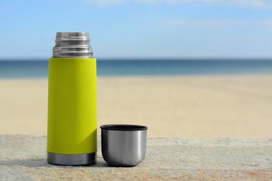 Photo of Metallic thermos and cap on stone surface near sea, space for text
