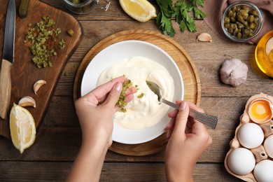 Photo of Woman making delicious tartar sauce at wooden table, top view