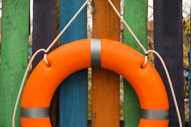 Photo of Orange lifebuoy hanging on color wooden fence, closeup. Rescue equipment