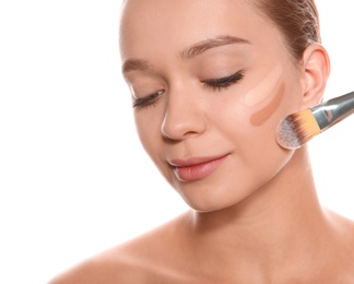 Photo of Young woman applying foundation on her face against white background