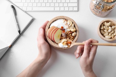 Photo of Woman eating tasty granola at workplace, top view