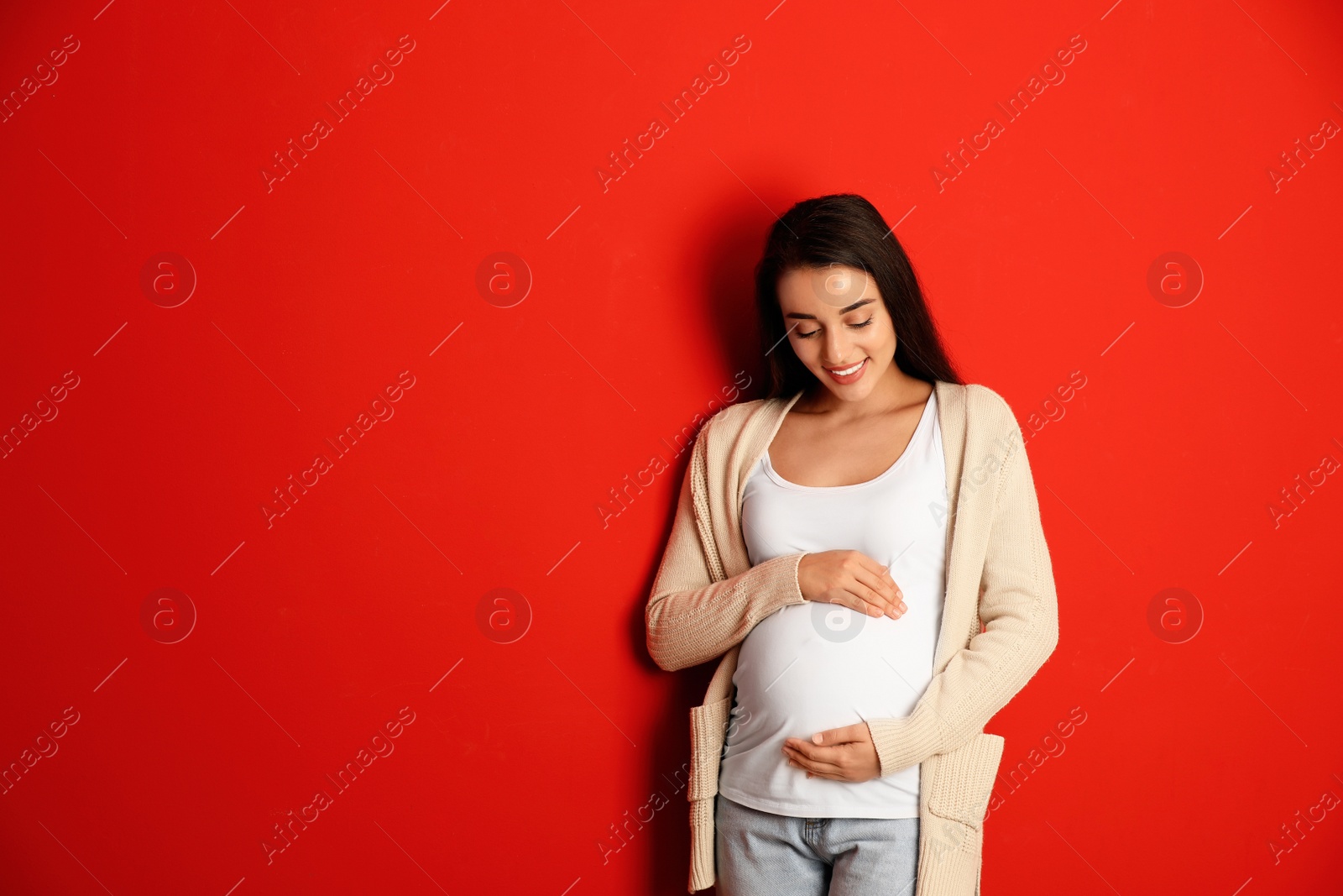 Photo of Happy pregnant woman on red background, space for text. Expecting baby