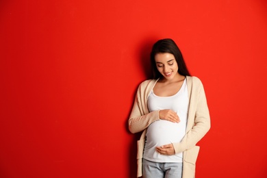 Happy pregnant woman on red background, space for text. Expecting baby