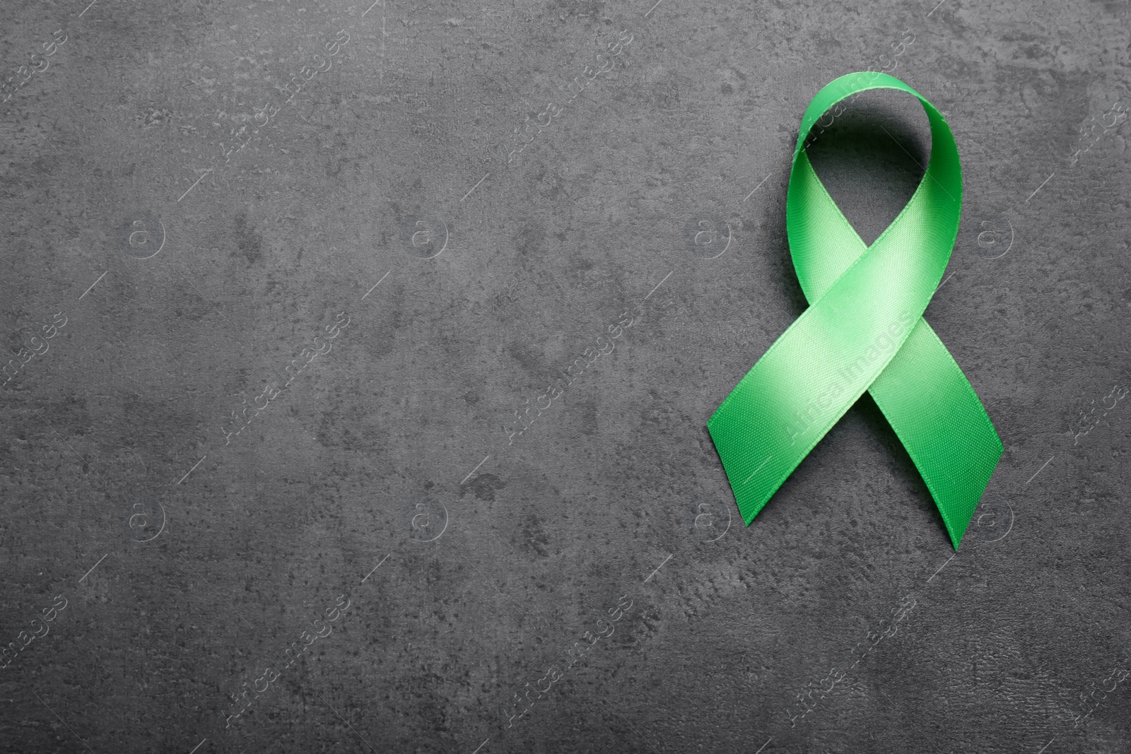 Photo of World Mental Health Day. Green ribbon on black background, top view with space for text