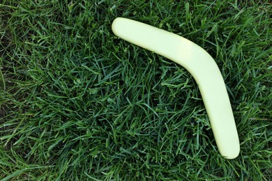 Light wooden boomerang on green grass outdoors, above view. Space for text