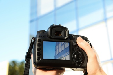 Photo of Female photographer holding professional camera with picture on screen outdoors, closeup