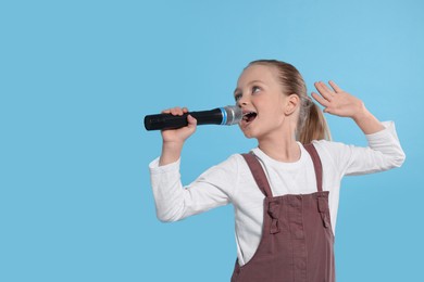 Cute little girl with microphone singing on light blue background, space for text