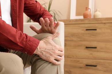 Senior man suffering from pain in his knee at home, closeup. Arthritis symptoms