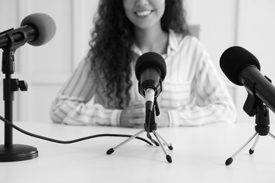 Journalist conference. Businesswoman giving interview at table with microphones indoors, closeup. Black and white effect