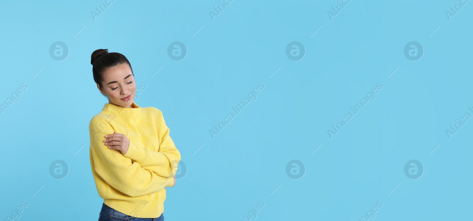Photo of Beautiful young woman wearing yellow warm sweater on light blue background. Space for text