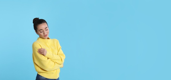 Photo of Beautiful young woman wearing yellow warm sweater on light blue background. Space for text