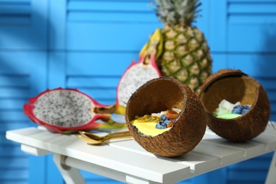 Tasty smoothie bowl served in coconut shells on white wooden table