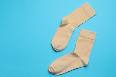 Photo of Beige socks on light blue background, flat lay. Space for text