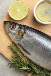 Photo of Wooden board with salted herring, lime, oil and rosemary on grey table, top view