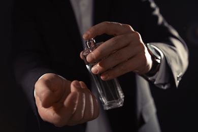 Man applying perfume on wrist against black background, closeup