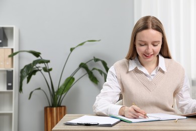 Woman taking notes at wooden table in office, space for text