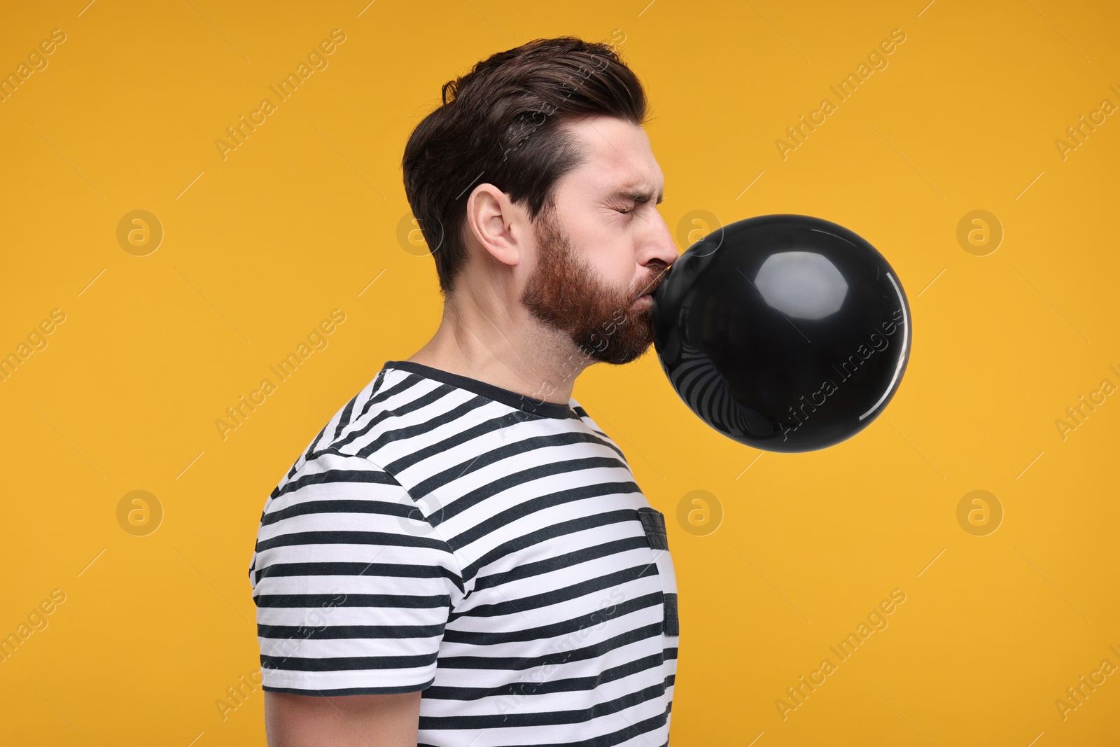 Photo of Man inflating black balloon on yellow background