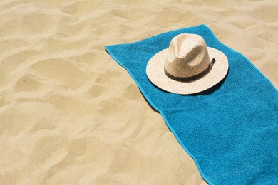 Photo of Soft blue towel and straw hat on sandy beach, space for text
