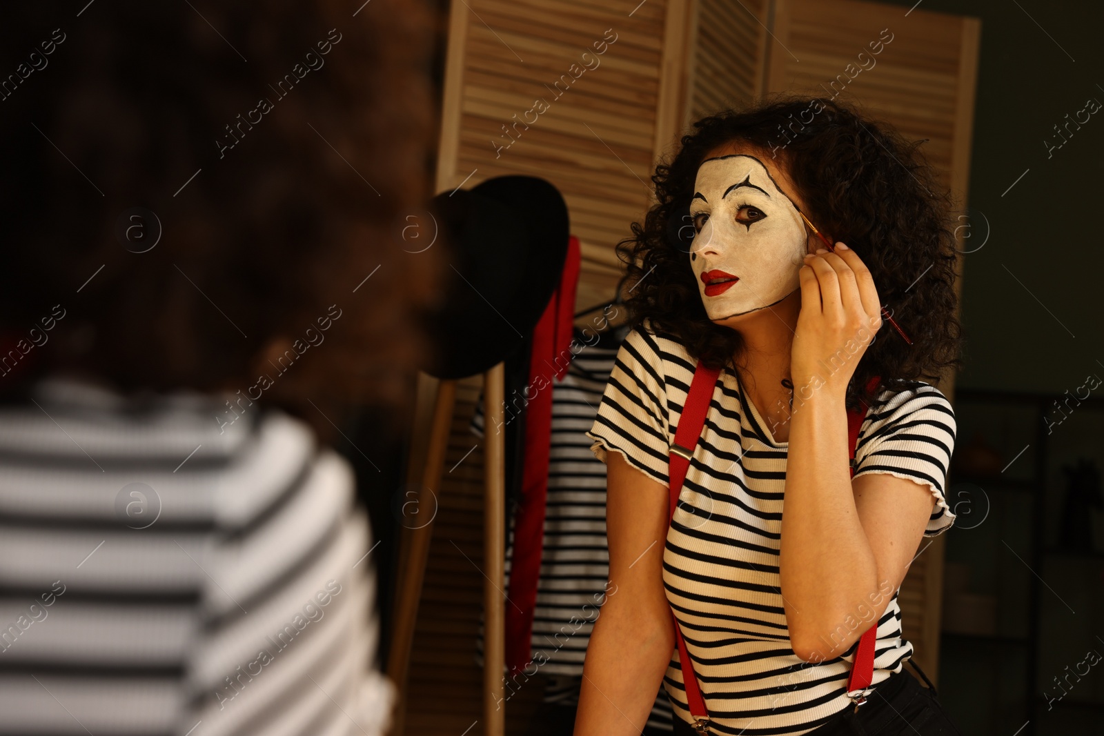 Photo of Young woman applying mime makeup near mirror indoors