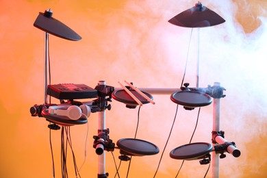 Photo of Modern electronic drum kit and smoke on orange background. Musical instrument