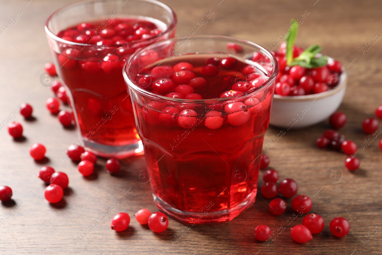 Photo of Tasty cranberry juice in glasses and fresh berries on wooden table, closeup