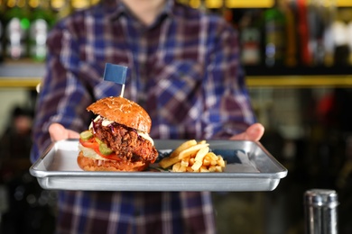 Photo of Man holding tray with delicious burger and french fries indoors, closeup