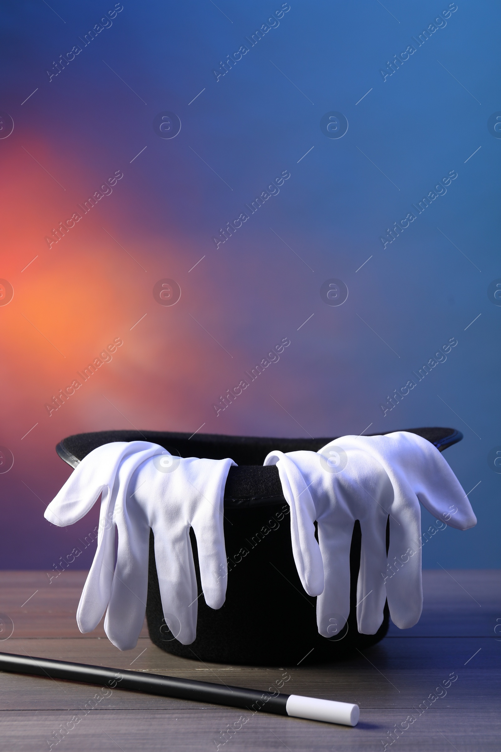 Photo of Magician's hat, wand and gloves on wooden table against color background, space for text